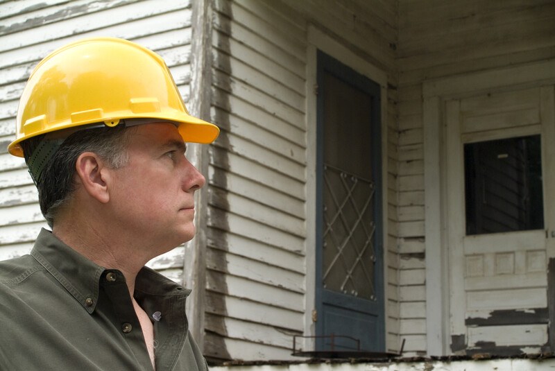 这张照片显示了一个戴着黄色安全帽的严肃的男人看着破败的白宫外面。